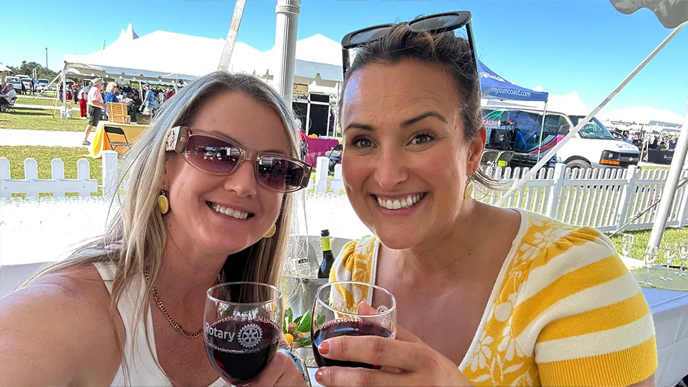 Two women smiling and toasting with red wine glasses at the Suncoast Food & Wine Fest.