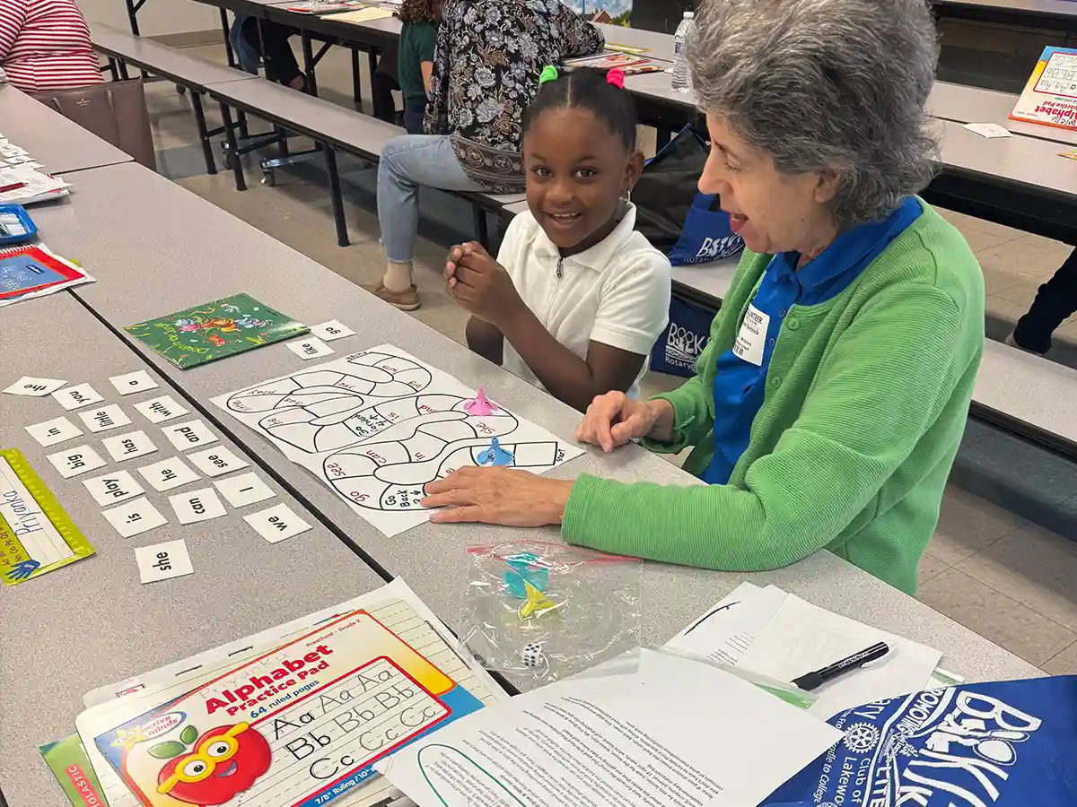 A young student and an adult volunteer playing a reading game together at a school table.