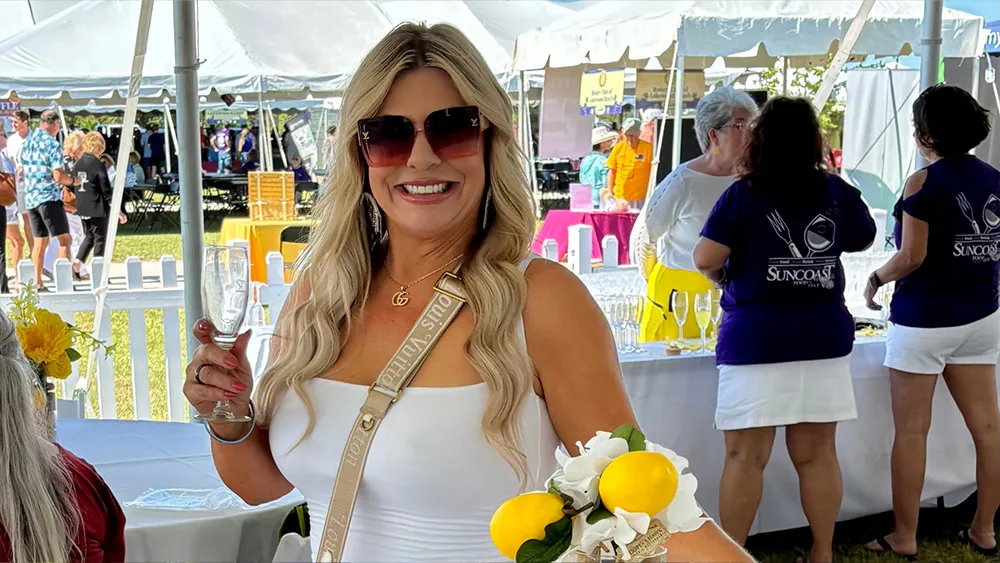 A smiling blonde woman holding a tasting glass at the Suncoast Food & Wine Fest.